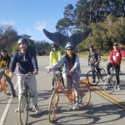 Students on bikes on Car-Free JFK in Golden Gate Park. A whale tail sculpture is in the background.
