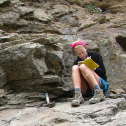 Student writing field notes while rock sampling
